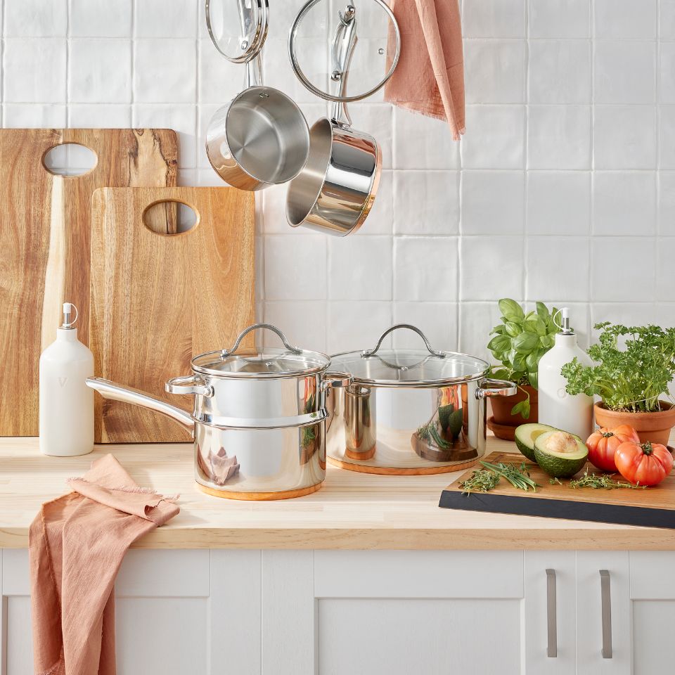 Stainless steel cookware and chopping boards on a wooden kitchen counter